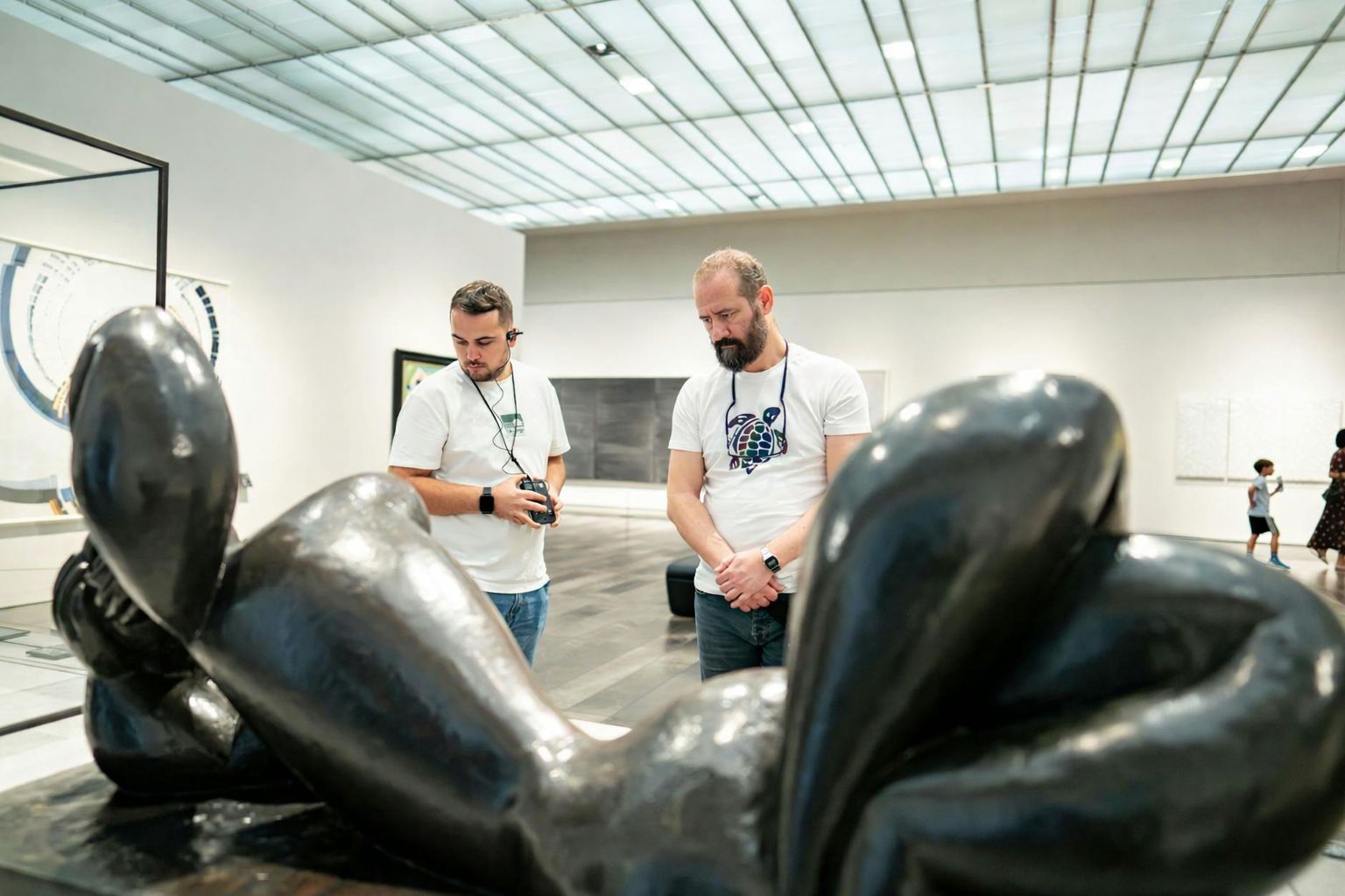 Två män betraktar en skulptur i ett museum, lyssnande på ljudguider.